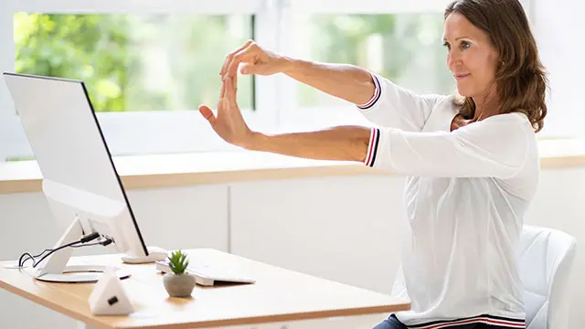 Kvinna som stretchar sittandes på sin arbetsplats framför datorn