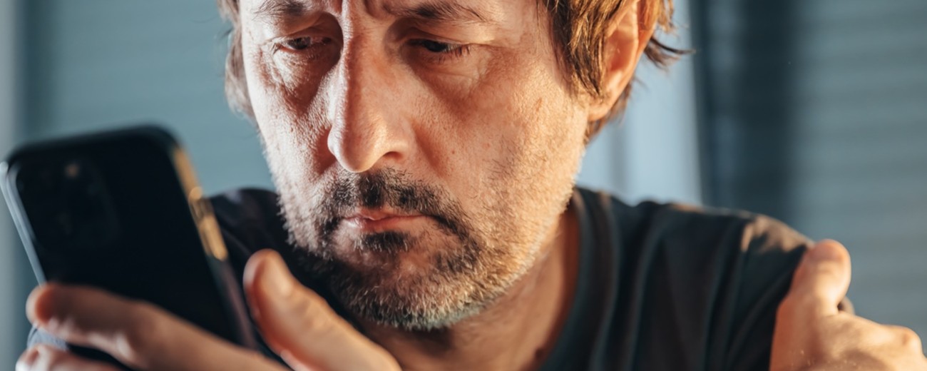 Person sitter i köket och tittar ner på sin mobiltelefon