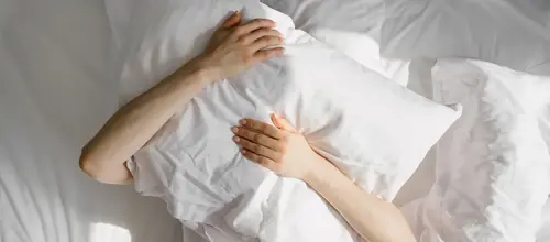 En person som ligger i säng och kramar om en kudde framför ansiktet