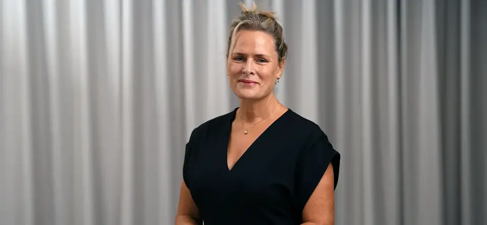 Malin Edlund står klädd i svart mot grå bakgrund och tittar leende in i kameran