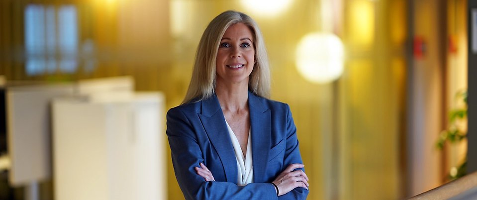 Ulrika står i kontorslandskap i blå kavaj och tittar leende in i kameran