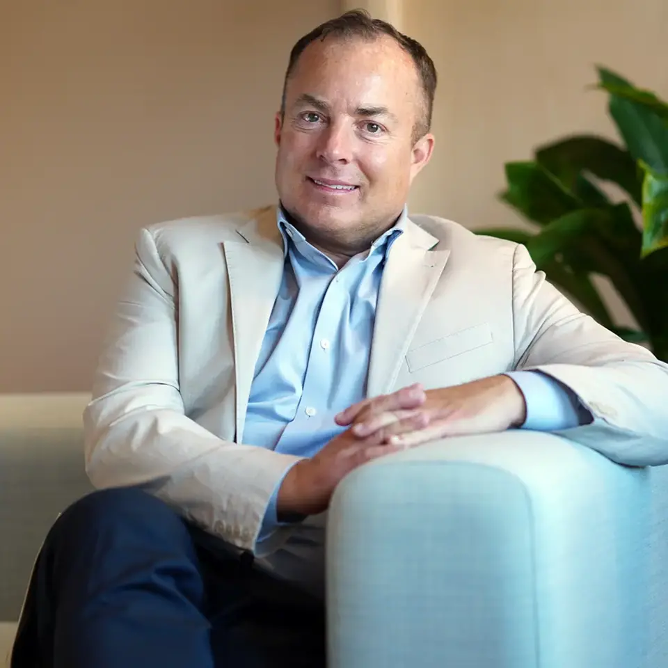 Fredrik Bengtsson sitter i soffa med ljus kostym, benen i kors och händerna i knät. Han lutar sig över soffkanten, ler och tittar in i kameran.