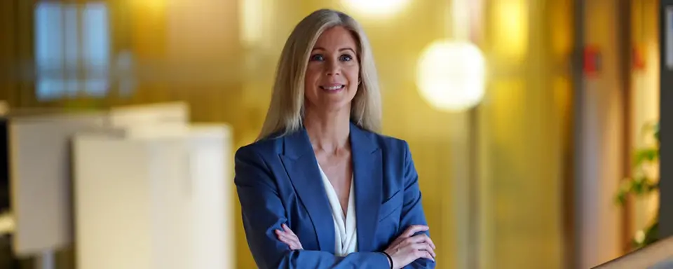 Ulrika står i kontorslandskap i blå kavaj och tittar leende in i kameran