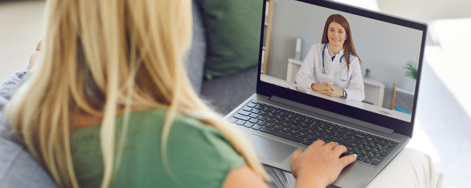 Kvinna sitter i soffa och träffar en läkare digitalt via laptop som hon har i knät