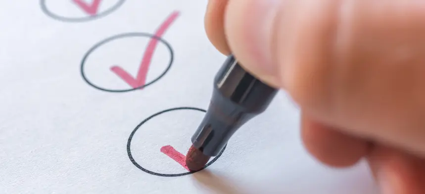 En hand som håller i en penna som bockar av en checklista.